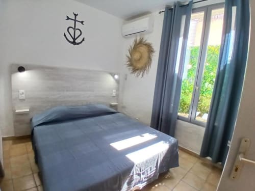 Comfortable double bedroom at Hôtel Quai d'Azur, Le Grau-du-Roi, with blue bedding, garden view doors, and nautical décor