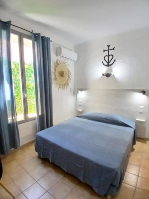 Comfortable double bedroom at Hôtel Quai d'Azur in Le Grau-du-Roi with blue bedding, white walls, and garden view doors