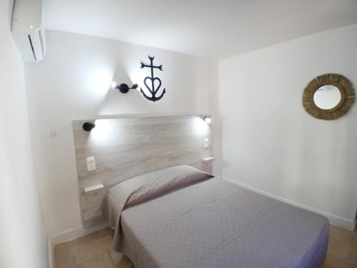 Modern bedroom at Hôtel Quai d'Azur with wooden headboard, white walls, decorative cross, and round mirror in Le Grau-du-Roi