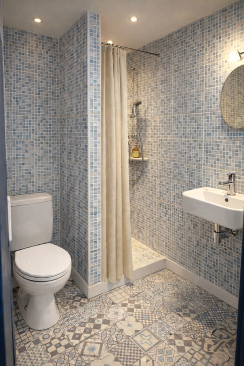 Modern bathroom with blue mosaic tiles, walk-in shower, white sink, and decorative floor at Hôtel Quai d'Azur, Le Grau-du-Roi