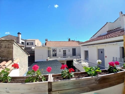Hôtel Quai d'Azur courtyard with pink flowers, white buildings, and striped terrace in Le Grau-du-Roi