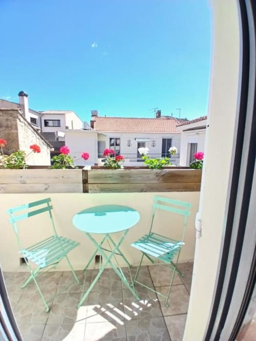 Turquoise bistro chairs and table on sunny balcony overlooking Le Grau-du-Roi courtyard at Hôtel Quai d'Azur