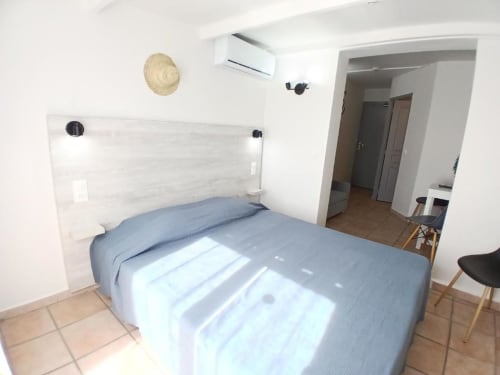 Modern bedroom at Hôtel Quai d'Azur in Le Grau-du-Roi with blue bedding, whitewashed headboard, and open doorway
