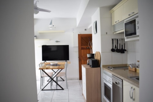 Modern Costa Adeje apartment kitchen and living area with TV, white cabinetry, stainless steel appliances, and wooden accents
