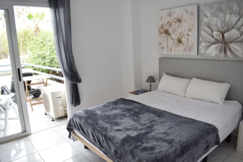 Modern bedroom in Costa Adeje apartment with gray headboard, white linens, dark throw blanket, and access to private terrace