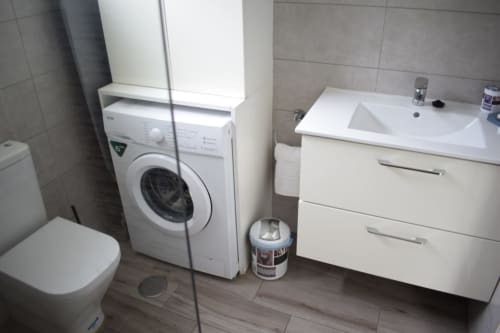 Modern bathroom with washing machine, white sink vanity, toilet, and tiled walls in Costa Adeje apartment