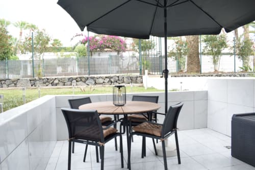 Modern apartment terrace in Costa Adeje with round dining table, black chairs, umbrella, and white tile patio overlooking