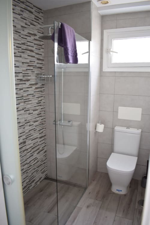Modern bathroom in Costa Adeje apartment with walk-in shower, striped tile accent wall, toilet, and purple towel