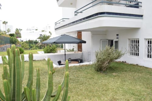 Modern white apartment in Costa Adeje, Tenerife with private patio, cacti garden, and black umbrella over seating area