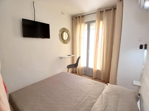 Double bedroom at Hôtel Quai d'Azur with bed, wall-mounted TV, chair, and French doors opening to terrace