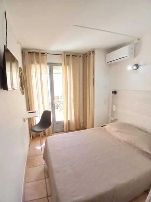 Modern hotel room at Hôtel Quai d'Azur with queen bed, beige curtains, balcony access, and air conditioning in Le Grau-du-Roi