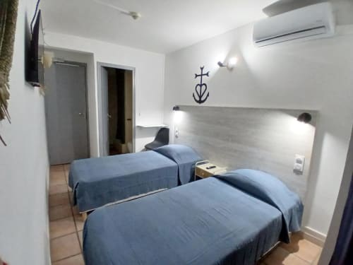Twin beds in modern hotel room at Hôtel Quai d'Azur, Le Grau-du-Roi with white walls and AC unit