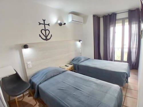 Twin beds in modern hotel room at Hôtel Quai d'Azur, Le Grau-du-Roi with balcony view and purple curtains