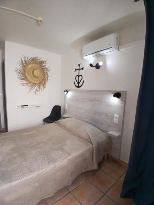 Modern double bedroom at Hôtel Quai d'Azur with gray headboard, straw wall art, and AC unit