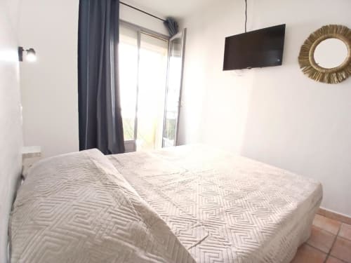 Bright bedroom at Hôtel Quai d'Azur with double bed, wall-mounted TV, balcony doors, and decorative mirror