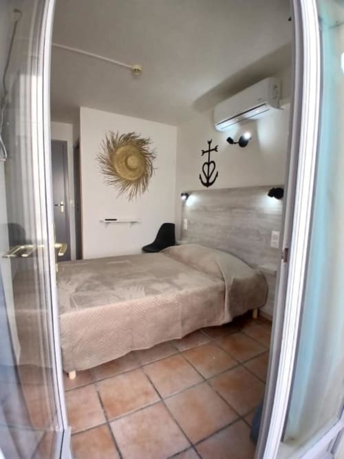 Modern double bedroom at Hôtel Quai d'Azur with beige bedding, white walls, decorative straw hat and nautical wall art, air
