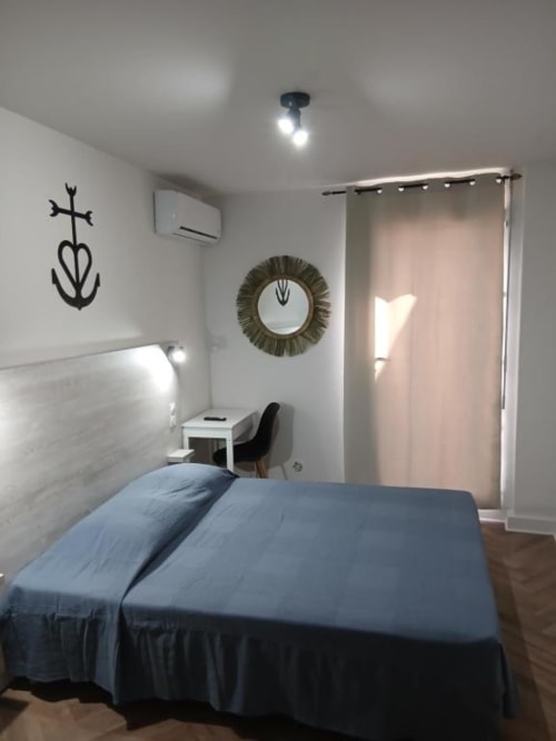 Modern hotel bedroom at Hôtel Quai d'Azur with blue bed, white headboard, round mirror, and minimalist decor