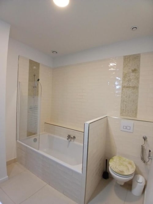 Modern bathroom at Hôtel Quai d'Azur with bathtub, glass shower screen, toilet, and beige tile walls