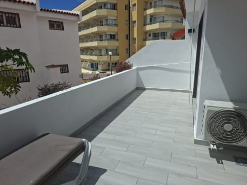Sunny balcony with tiled terrace, white walls, AC unit, and views of surrounding apartment buildings in Costa Adeje, Tenerife