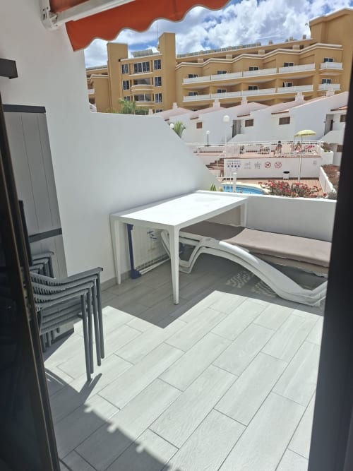 Sunny private balcony with white table, loungers, and red awning overlooking Costa Adeje resort pool and apartments