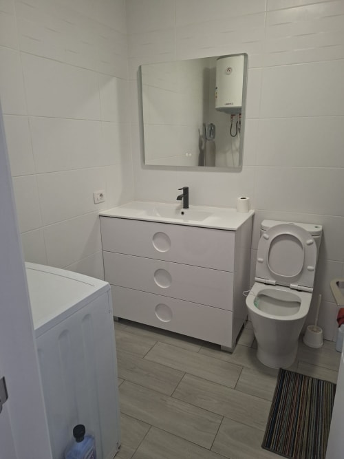 Modern bathroom in Costa Adeje apartment with white vanity, sink, toilet, mirror, and tiled walls and flooring.