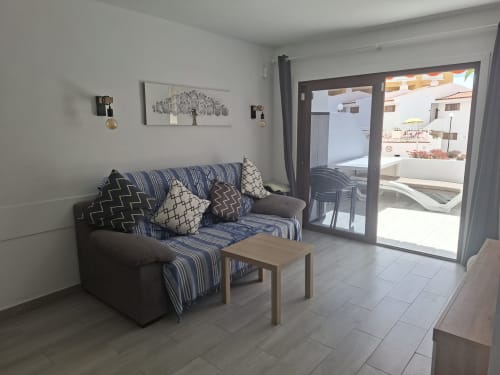 Modern living room with striped sofa, wooden table, and glass doors opening to balcony in Costa Adeje apartment