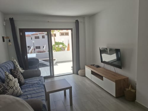 Modern living room in Costa Adeje apartment with blue striped sofa, flat-screen TV, dining table, and balcony doors