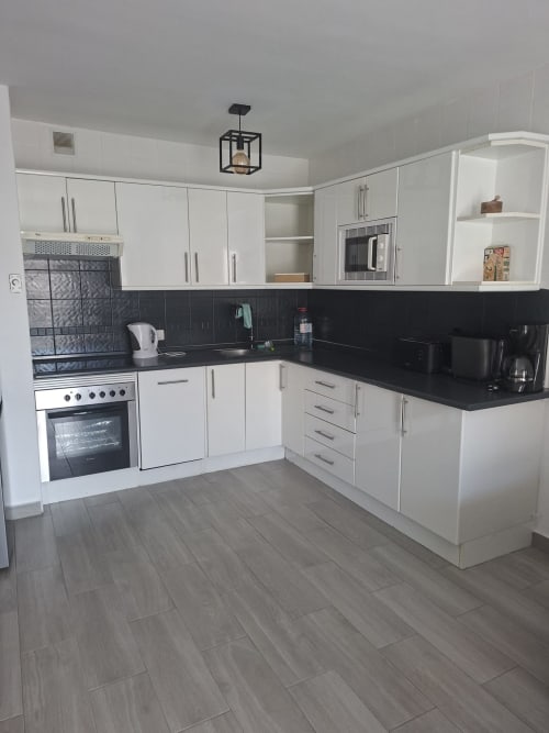 Modern white kitchen with black countertops and wood flooring in Costa Adeje apartment, featuring stove, oven, and full
