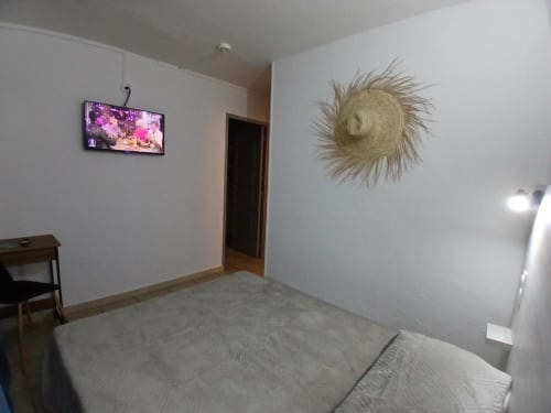 Modern hotel bedroom at Hôtel Quai d'Azur with bed, wall-mounted TV, decorative straw hat, and dark wooden door