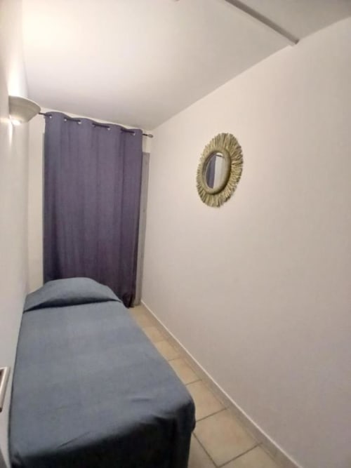 Compact bedroom with single bed, purple curtains, and gold circular mirror at Hôtel Quai d'Azur, Le Grau-du-Roi
