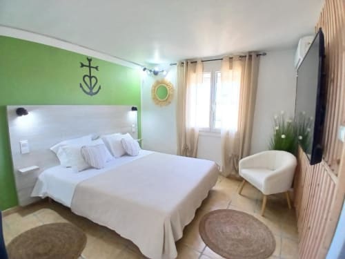 Modern hotel bedroom at Hôtel Quai d'Azur with green accent wall, white bed, beige curtains and contemporary furnishings