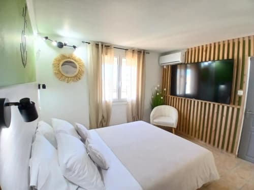 Hôtel Quai d'Azur love room with white bed, wooden accent wall, TV, and beige curtains in Le Grau-du-Roi