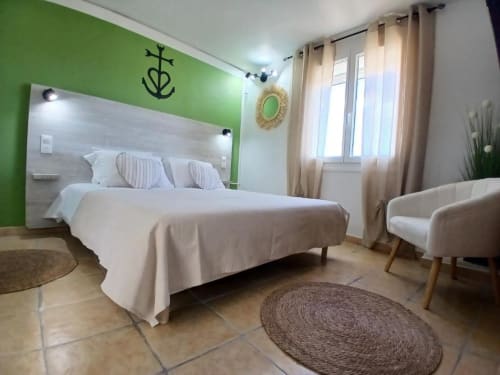 Bright green accent wall in modern bedroom at Hôtel Quai d'Azur, Le Grau-du-Roi, with white bedding and beige curtains