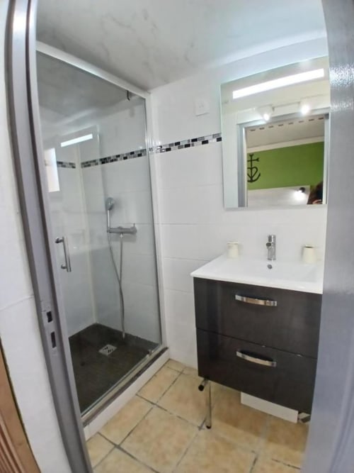 Modern bathroom at Hôtel Quai d'Azur with black vanity, glass shower enclosure, and decorative tile border