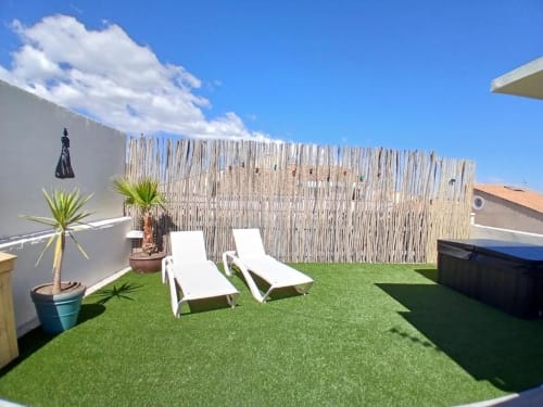 Rooftop terrace at Hôtel Quai d'Azur with lounge chairs, artificial grass, palm plants and wooden privacy screen
