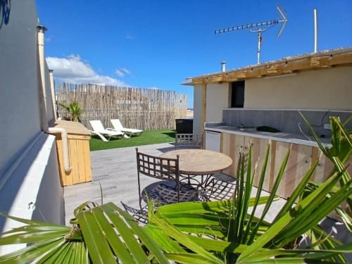 Rooftop terrace with dining table, lounge chairs, outdoor kitchen, and lush plants at Hôtel Quai d'Azur in Le Grau-du-Roi
