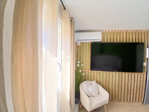 Modern hotel room at Hôtel Quai d'Azur with cream armchair, wooden wall paneling, TV, and air conditioning unit
