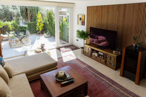 Moderno salón con televisor, chimenea, sofá crema y vista al jardín del hotel BH Marbella en España