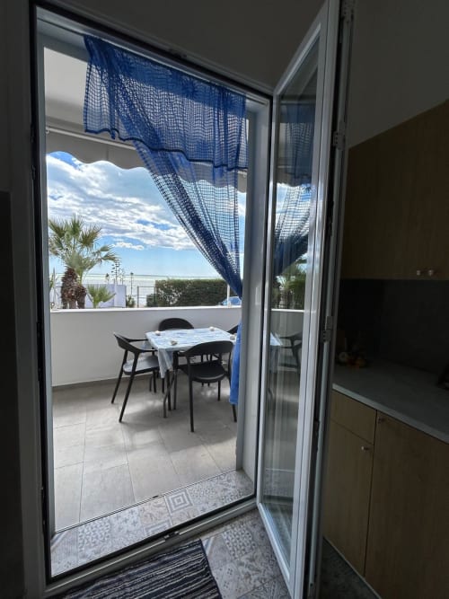 Balcone con vista mare a Sostare a Gela, tavolo da pranzo, tende blu e panorama costiero di Gela oltre la ringhiera.