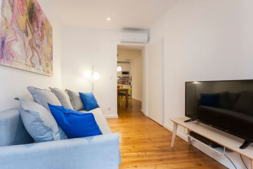Sala de estar de apartamento moderno em Lisboa com sofá azul, TV de ecrã plano, pavimento de madeira e decoração minimalista no Bairro Alto