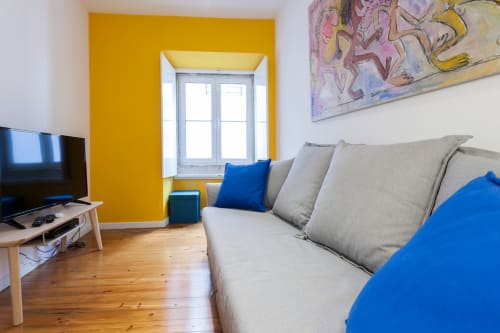 Sala de estar moderna no Bairro Alto com sofá bege, almofadas azuis, parede amarela, pisos de madeira e televisão plana