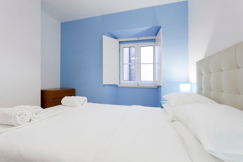 Quarto luminoso no apartamento do Bairro Alto com parede azul, duas camas de solteiro, roupa de cama branca e luz natural da janela