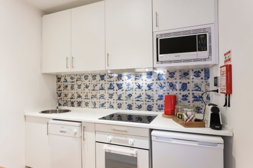 Cozinha moderna em apartamento do Bairro Alto com armários brancos, azulejo azul, micro-ondas, máquina de lavar louça e aço inoxidável