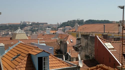 Vista de telhados do Bairro Alto com telhas de barro, edifícios históricos de Lisboa e paisagem urbana ao fundo