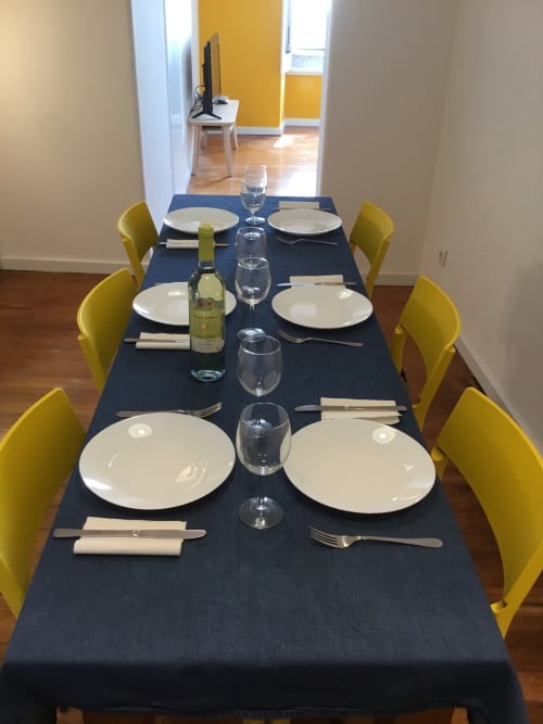 Mesa de jantar formal com cadeiras amarelas, pratos brancos, taças de vinho e garrafa de vinho branco no Lisbon Heart Pulse Stays