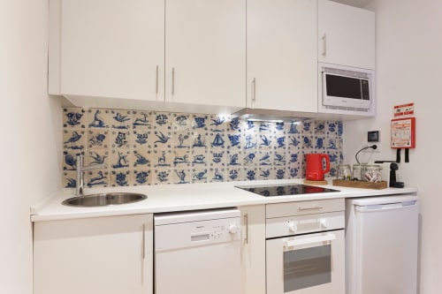 Cozinha moderna branca com azulejo padrão azul, placa de indução, forno e máquina de lavar louça em apartamento de Lisboa