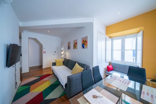Apartamento moderno em Lisboa, Bairro Alto, com tapete geométrico colorido, sofá cinzento, parede amarela e grandes janelas