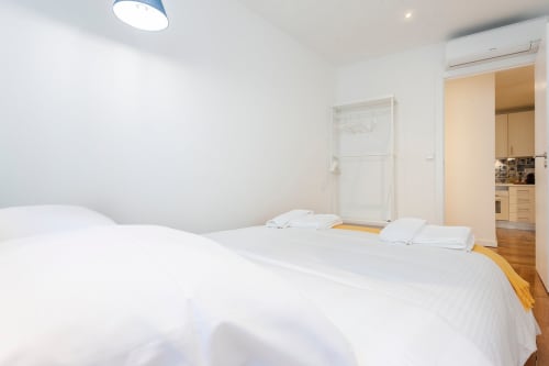 Quarto moderno e luminoso em apartamento de Lisboa com duas camas brancas, piso de madeira, kitchenette, ar condicionado e design minimalista
