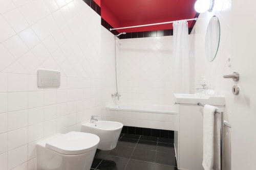 Casa de banho moderna com azulejos brancos, piso preto, teto com destaque vermelho, sanita, bidé, lavatório com espelho e chuveiro em Lisboa