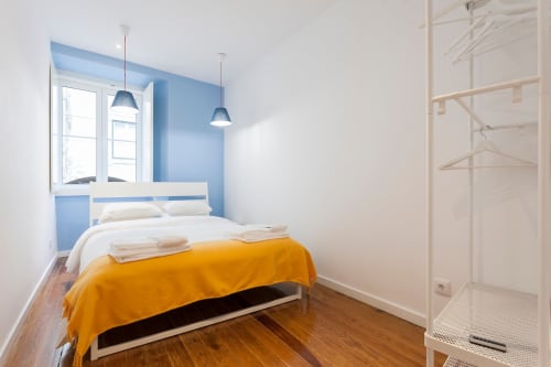 Quarto moderno no apartamento de Bairro Alto, Lisboa, com parede de destaque azul, roupa de cama amarela, assoalho em madeira e iluminação pendente